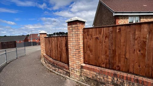 wooden fence and brick columns along a walkway in a suburban area with houses in the background showcasing three distinct architectural features