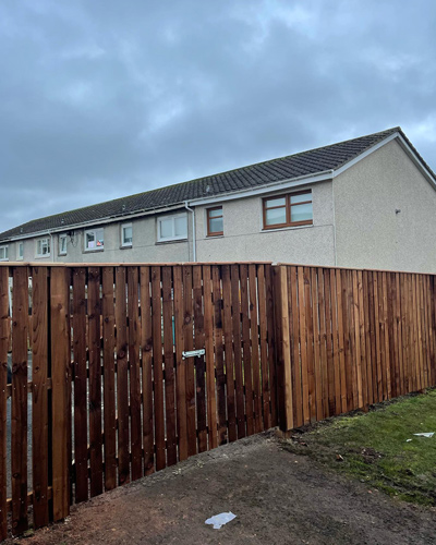 wooden fence enclosing house with cloudy sky two stories and grassy area