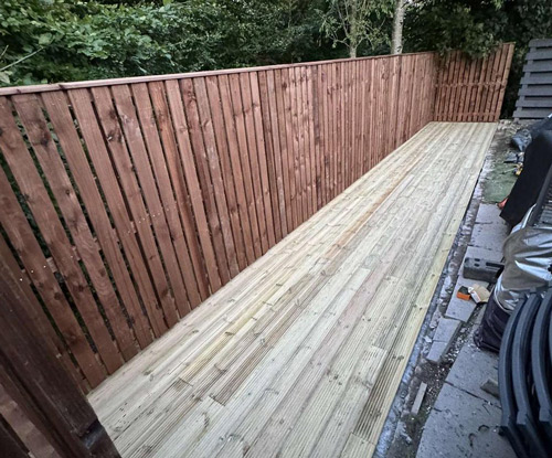 wooden fence and deck area with three planks creating a smooth surface and vertical slats surrounded by greenery